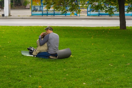 DNEPR, UKRAINE - SEPTEMBER 25, 2016:Young loving couple sitting on a ground pad on green lawn on Dnepr river embankment in center of Dnepr city at autumnal weekendのeditorial素材
