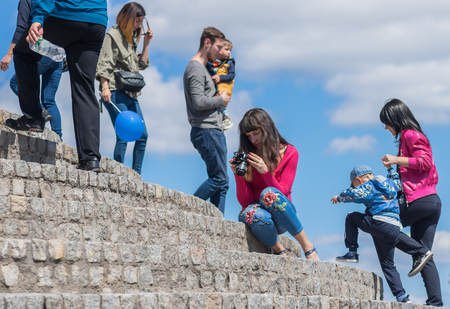 Dnipro, Ukraine - May 09, 2017: Caucasian young woman  sitting on stone footsteps and watching pictures from digital camera screen while people go  around.のeditorial素材