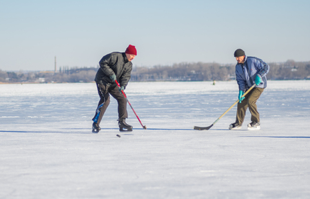 Dnipro, Ukraine - January 22, 2017: Two mature man fighting for the pack while playing amateur hockey on a frozen river Dnepr in Ukraineのeditorial素材