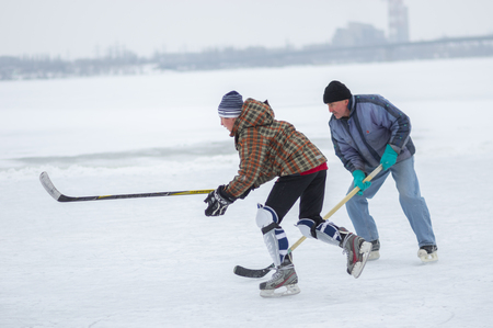 Dnipro, Ukraine - January 28, 2018: Young man fight with old man for the puck while playing hokey on a frozen river Dnipro in Ukraineのeditorial素材