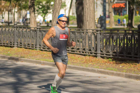 DNIPRO, UKRAINE - SEPTEMBER 26, 2021: Lonely senior man running on an empty city street during 42 km distance of Almaz group Dnipro Marathonのeditorial素材