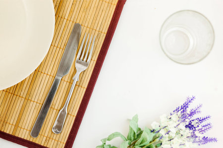 A dish with folk and knife on a bamboo plate matt with glass and flowersの写真素材