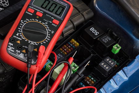 Auto service, repair and maintenance concept - digital multimeter or voltmeter testing car battery.
