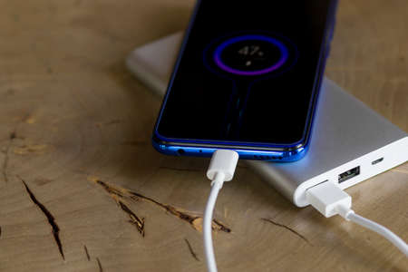 Smartphone charging battery from external power bank in outdoor. Wooden background.