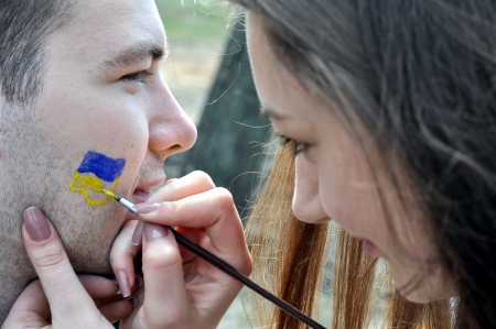 young woman - body art painter painting ukrainian flag  on the male