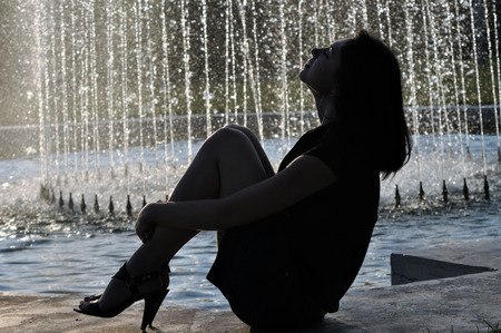 attractive woman relaxing near the fountain in hot day, back litの写真素材