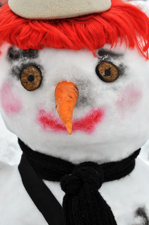 close-up of snow man with red wig, black scarf and bonnetの写真素材