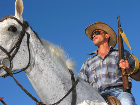 portrait of young  ranger horseback riding with rifle in the sunny dayの写真素材