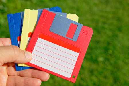 Vintage colored floppy disks in a hand on green grass lawn background. Old technologiesの写真素材