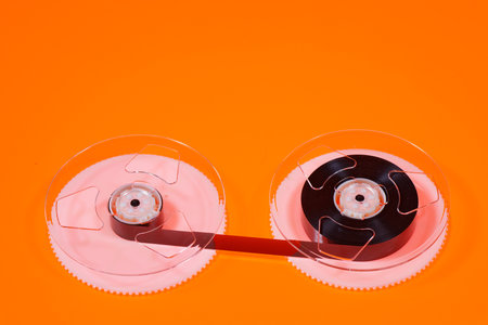 Magnetic tape on reels from a VHS videocassette on orange backgroundの写真素材