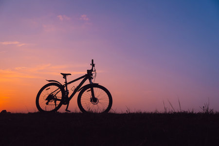 Silhouette of mountain bike on the grass with sunset sky backgroundの写真素材