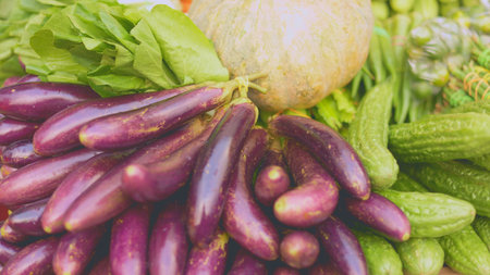 Fresh vegetables piled on stall vendor arranging colorful display of eggplant, cucumber, long beans and cabbage in wooden crate under warm morning light, rustic market atmosphere and vivid texturesの写真素材