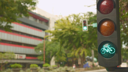 Traffic light green bicycle signal clears path for group riders on city street, small convoy of cyclists pass office block, bright daytime scene, big city conceptの写真素材