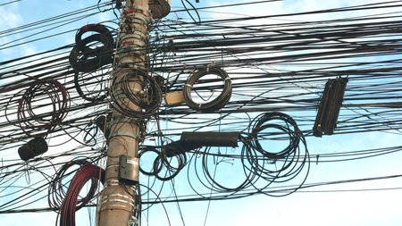 Massive coil bundles crowd utility pole junction with metal brackets and dangling loops, tangled...