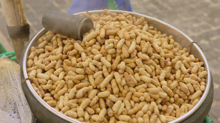 Roasted peanut stall, vendor serves freshly roasted peanuts, closeup of vendor preparing roasted...
