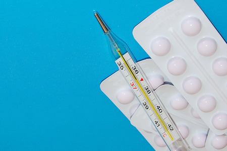 Many packs of pills and a medical thermometer. Tablets are next to the packaging on a blue background. copyspaceの写真素材