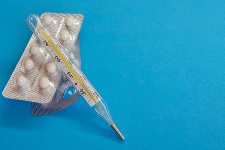 Medical thermometer and white pills on a blue background. Tablets in the package on the table