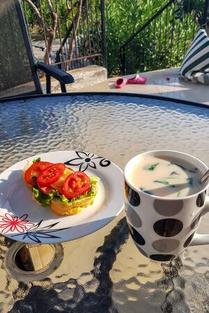 Breakfast from a sandwich with sausage, tomatoes, cheese, herbs and a cup of yogurt with fresh herbs.の写真素材