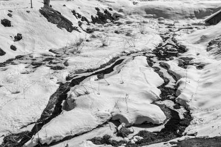 Streams running through snowdrifts. Black and white contrast photo.
