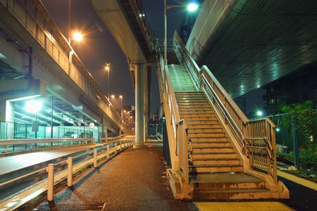 illuminated stairs going up between huge highway structures in night cityの写真素材