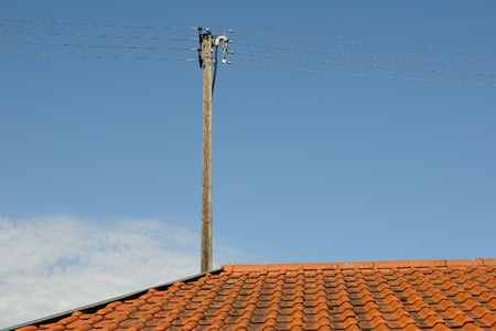old style red tiled roof with wire post over blue summer skyの写真素材