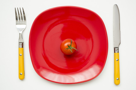 fresh small tomato fruit on red plate with cutleryの写真素材