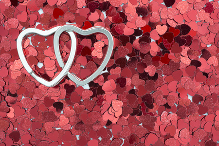 two linked metallic rings in shape of heart on the red confetti backgroundの写真素材