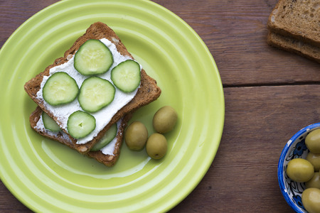 cheese toasts with cucumber slices and green olives on plateの写真素材