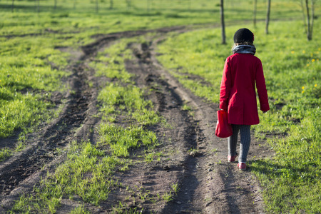 girl in red coat going far away by dirty country road, selective focus on girlの写真素材