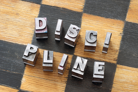 discipline word made from scattered metallic letterpress type  on wooden chessboardの写真素材