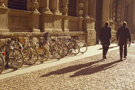 MILAN - OCTOBER 22: Two men walk by cobblestone pavement along bicycle parking by sunny morning in Milan, Italy on October 22, 2015.のeditorial素材