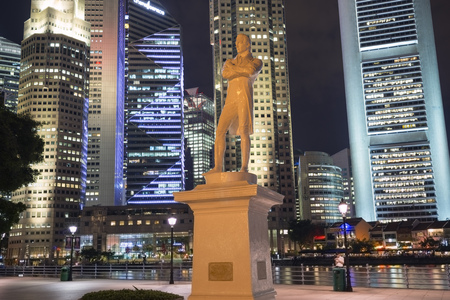 SINGAPORE - NOVEMBER 13,  2014: Statue of Sir Stamford Raffles (a founder of the city) illuminated by night at Raffles' Landing Site with downtown buildings in Singapore on November 13, 2014.のeditorial素材