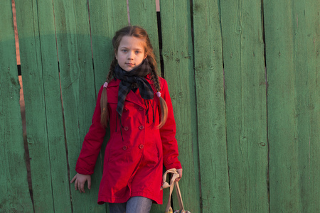 fashion girl in red raincoat posing near old wooden fence by eveningの写真素材