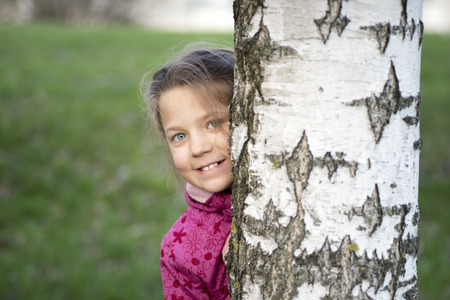 cheerful girl hiding behind birch stem by springの写真素材