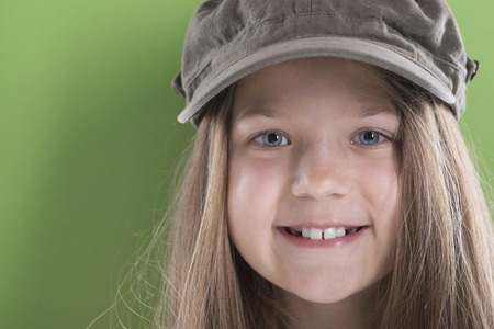 smiling girl face in peaked cap with long hairs over green backgroundの写真素材