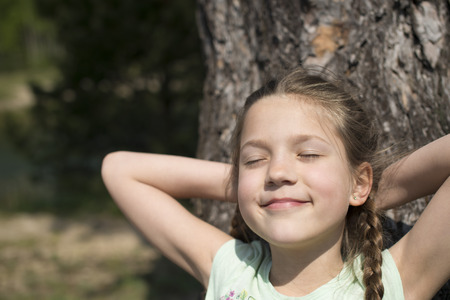 happy child girl sunbathing with closed eyes near huge treeの写真素材