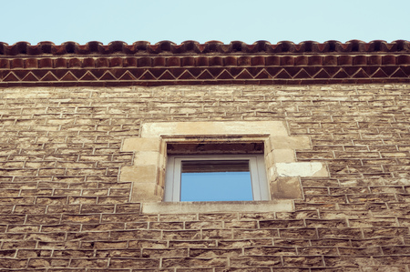 ancient brick wall fragment with small window, roof end and clear skyの写真素材