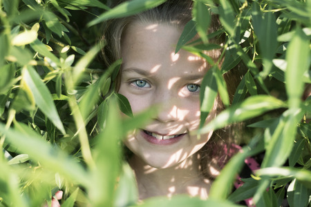 portrait of smiling girl behind many green leaves of willow treeの写真素材