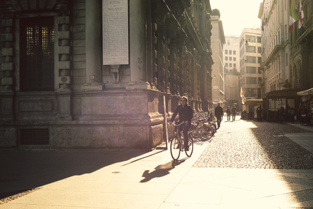 MILAN - OCTOBER 22: Men rides bicycle by cobblestone pavement along sunny street by morning in Milan, Italy on October 22, 2015.のeditorial素材