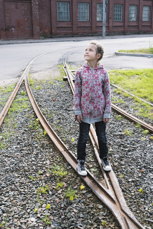 playful urban girl staying on rail tracks and looking upの写真素材