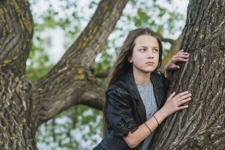 beautiful girl looking aside close to big tree trunk の写真素材