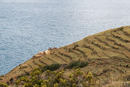 terraced fields and farm buildings on slope of Moon Island at lake Titicaca in Boliviaの写真素材