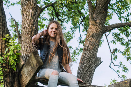 happy teenage girl sitting on wooden terrace arranged on tree branchesの写真素材
