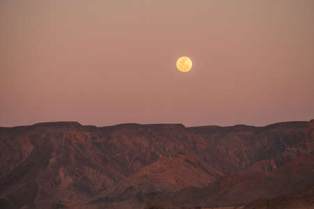 full moon above rocky mountain ridge in desert of Namibiaの写真素材