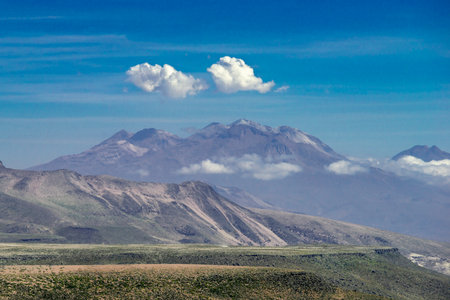 scenic mountain landscape in Peru with white clouds over volcano