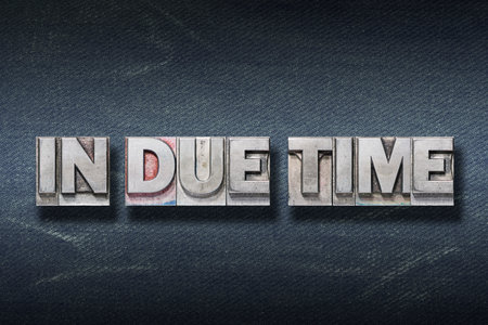 in due time phrase made from metallic letterpress on dark jeans backgroundの写真素材