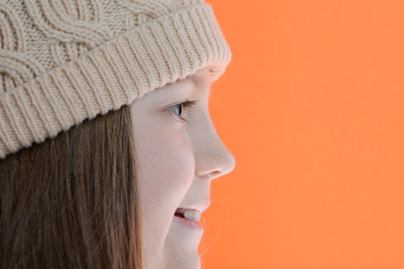 smiling girl in cap with long hairs side view over orange backgroundの写真素材