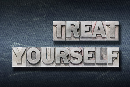 treat yourself phrase made from metallic letterpress on dark jeans backgroundの写真素材