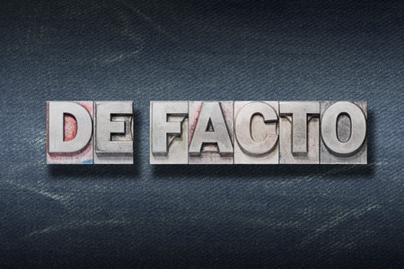 de facto (something that happens in practice) phrase made from metallic letterpress on dark jeans...