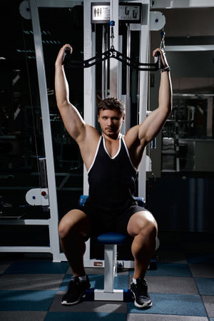 Muscular athletic young man fitness model do exercises in gym